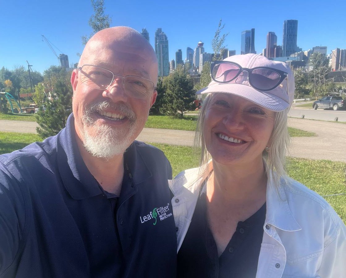 Steve and Inga smiling in a Calgary park with the downtown skyline behind them